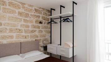 A bedroom with a stone wall, a bed with a brown headboard, a white bedside table with a towel, and a clothing rack.
