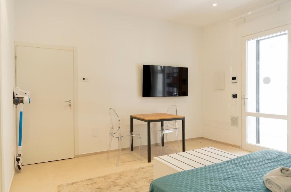 A bedroom with a bed, a TV mounted on the wall, a door, and a window.