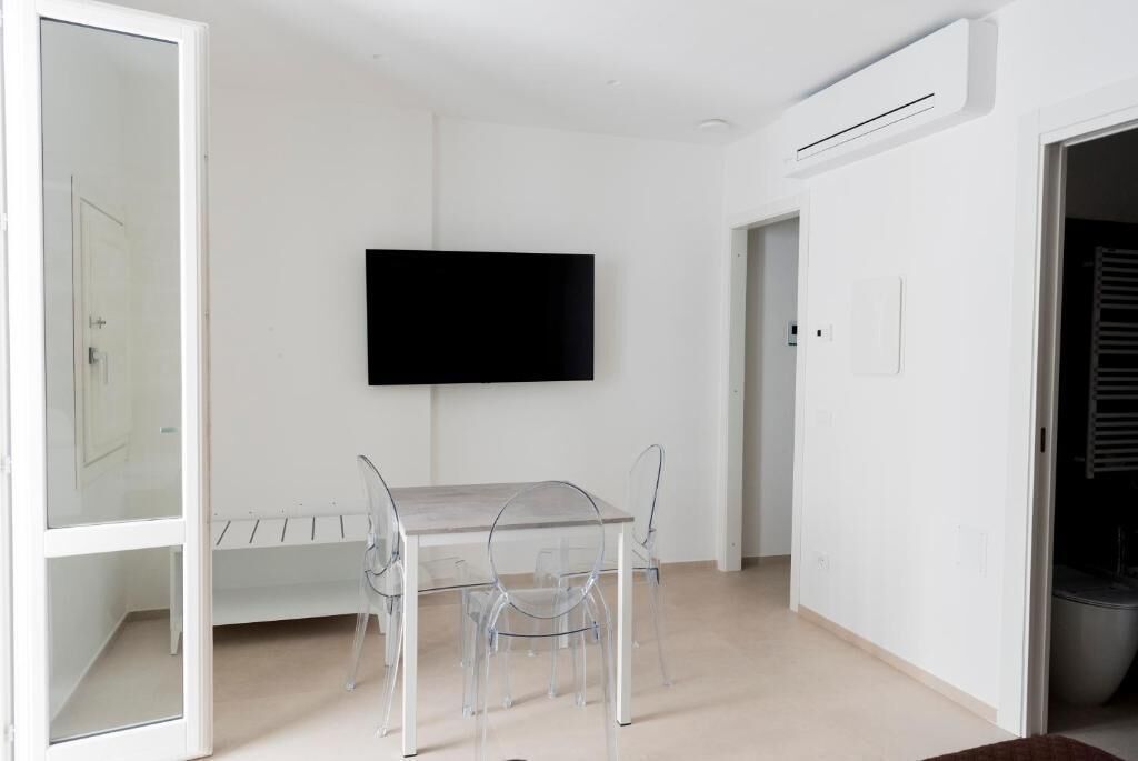 A room with a TV mounted on the wall, a dining table with chairs, and a visible door.