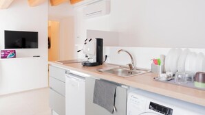 Una cocina moderna con lavavajillas, cafetera, pileta y un televisor de pantalla plana montado en la pared.