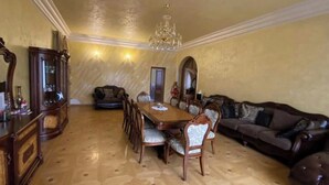 Ein Essbereich mit Holztisch und Stühlen, einer Kristallleuchtre, einem dunkelblauen Sofa und einer Vitrine mit Glastüren.