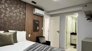 Een moderne slaapkamer met een groot bed, een airconditioningapparaat, een deur naar een badkamer en een klein bureau.