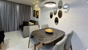Een moderne eetruimte met een marmeren tafel, grijs beklede stoelen en een wandlamp.