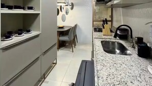 Een moderne keuken met grijze kastjes, een granieten aanrechtblad en een eethoek met tafel en stoelen.