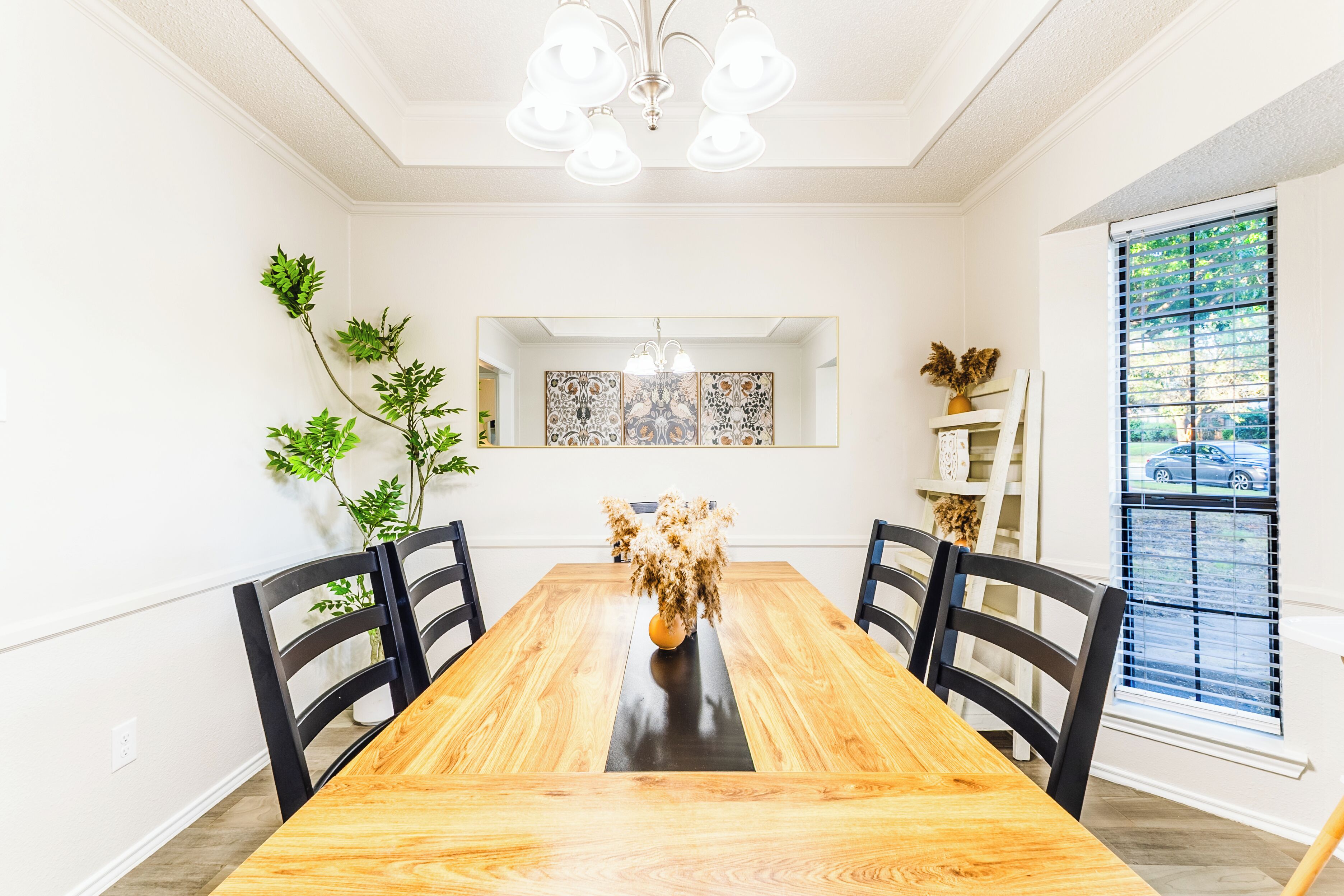 Ein Esszimmer mit Holztisch, schwarzen Stühlen, einer Kronleuchter und Wanddekoration.