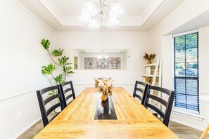 A dining room with a wooden table, black chairs, a chandelier, and decorative wall art. - Cozy Frisco Getaway - Fireplace + Relaxing Backyard (Frisco)