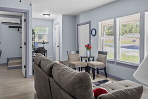 A living room with a grey sofa, a small round table with chairs, a clock on the wall, and a window with blinds. - Nonie's Hideaway is a quiet place to escape and unwind (Checotah)
