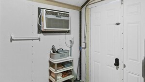 A room with a white door, a white wall-mounted air conditioner, a white shelf with folded towels, and a broom leaning against the wall. - Cozy Cottage - Direct access to Brimstone Trails - Multiple Hot Tubs- Fire Pits (Huntsville)