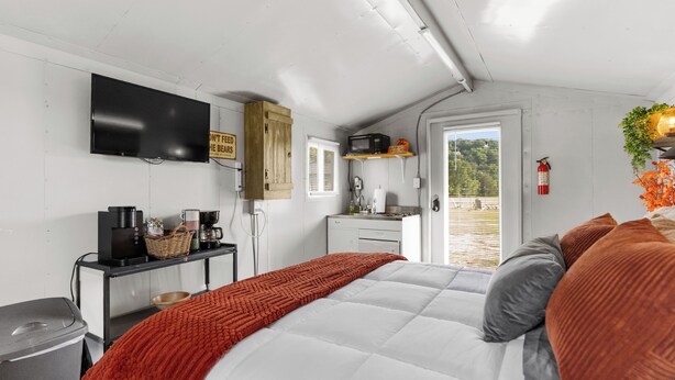 A bedroom with a bed, a television, a kitchenette, and a door leading to a balcony. - Cozy Cottage - Direct access to Brimstone Trails - Multiple Hot Tubs- Fire Pits (Huntsville)