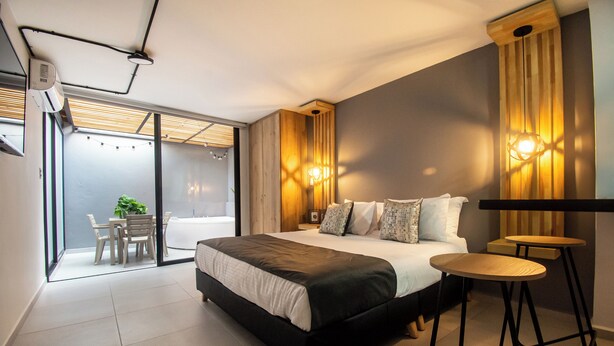 Une chambre moderne avec un grand lit, un coin repas avec des chaises et une vue à travers une porte vitrée.