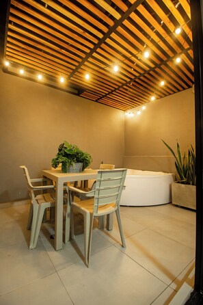 A modern interior with a wooden ceiling, a round table with chairs, a bathtub, and potted plants. - Barcelo Coliving (Medellín)