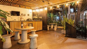 Un espace bar moderne avec un plafond à lattes de bois, des tabourets en béton et un comptoir où sont exposés divers objets.