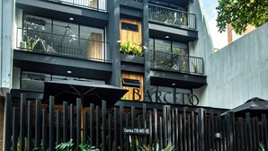 Un bâtiment moderne avec une clôture noire, des plantes en pot et une enseigne sur laquelle on peut lire « SARCELO ».