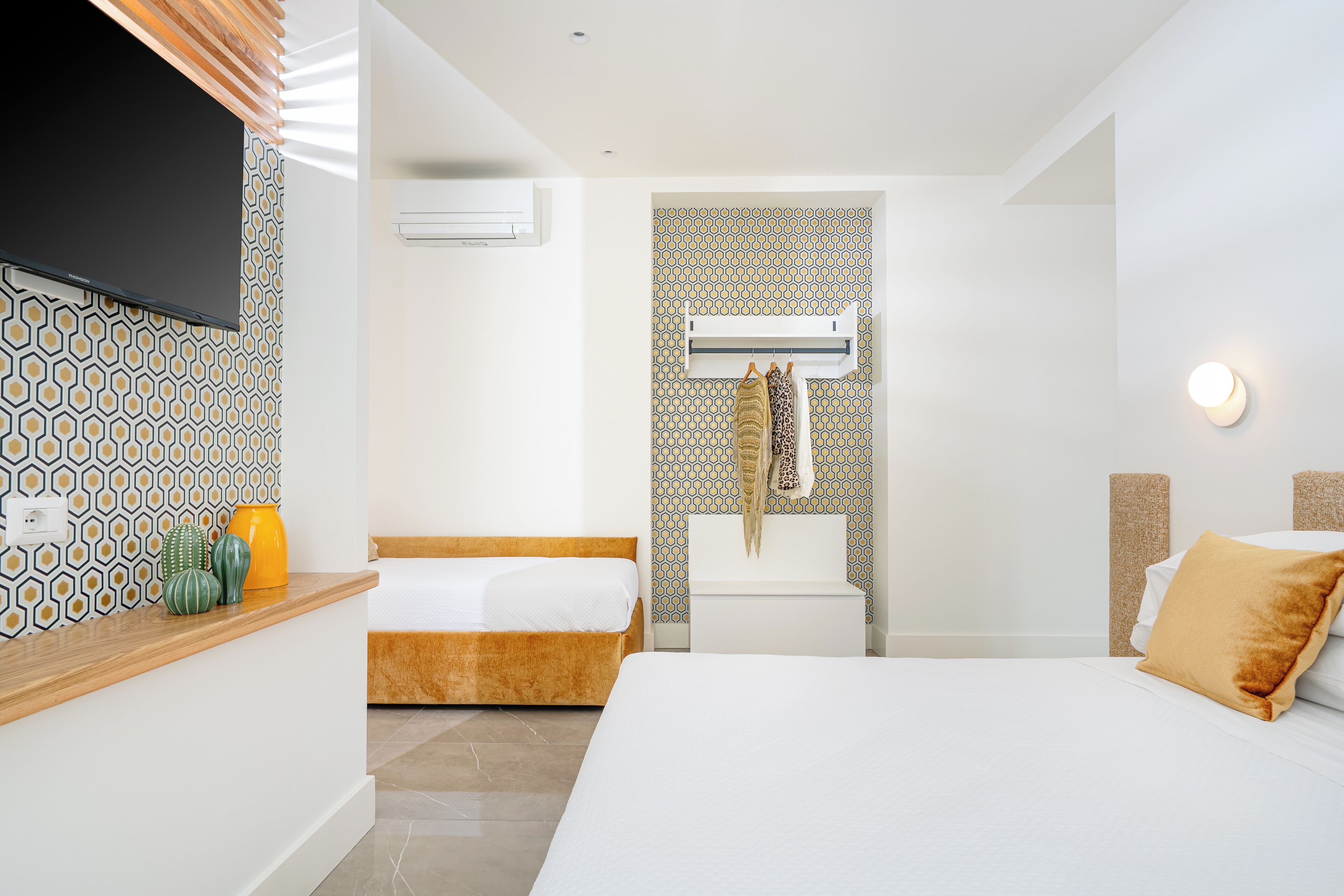 A hotel room with a bed, a bedside table, a TV, a bathroom with a toilet and sink, and patterned walls.