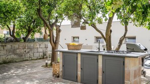 Un área de cocina al aire libre con estufa integrada, una cesta en la encimera y un muro de piedra al fondo.