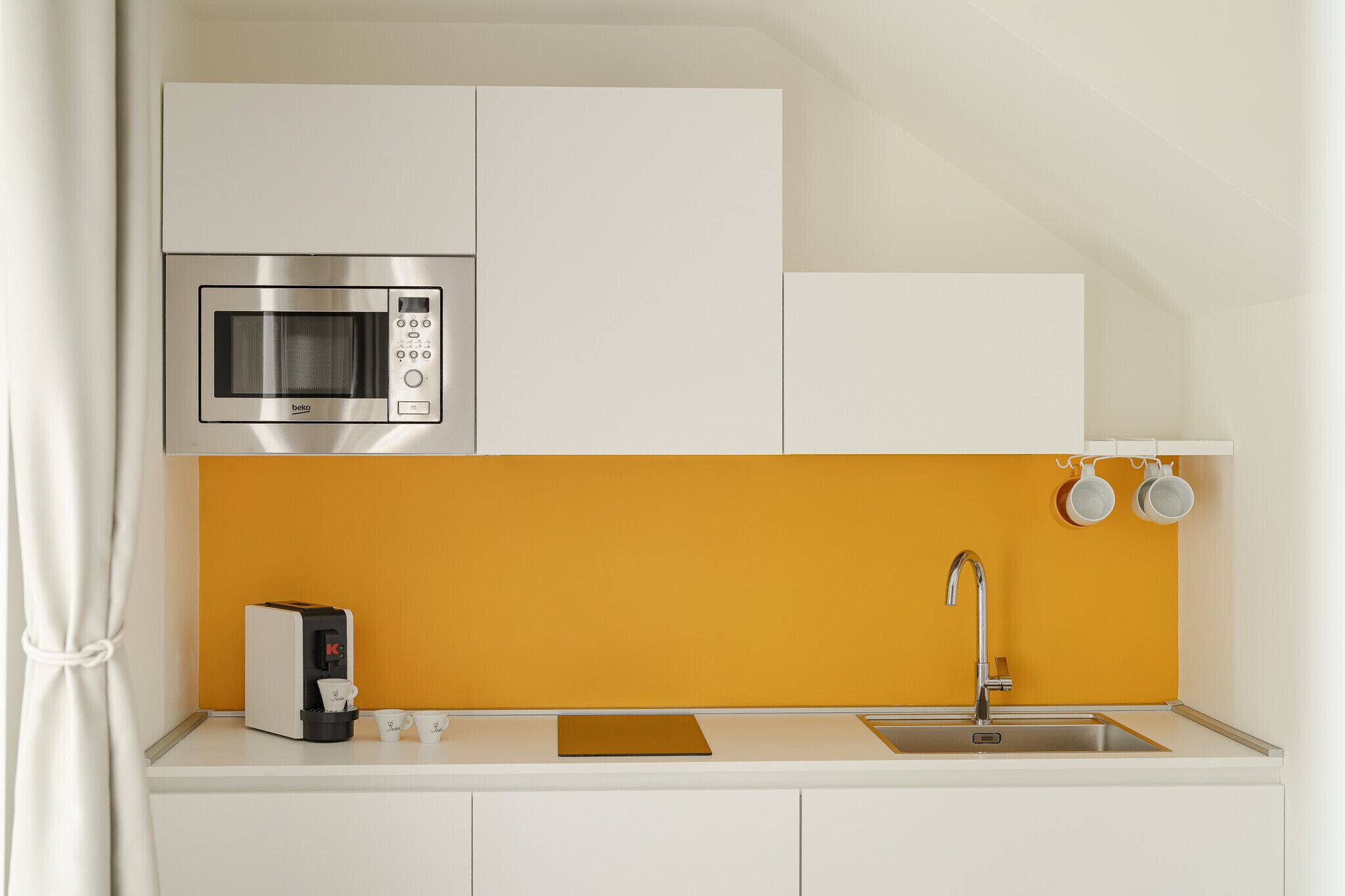 A kitchenette with a microwave, coffee machine, sink, and orange backsplash.