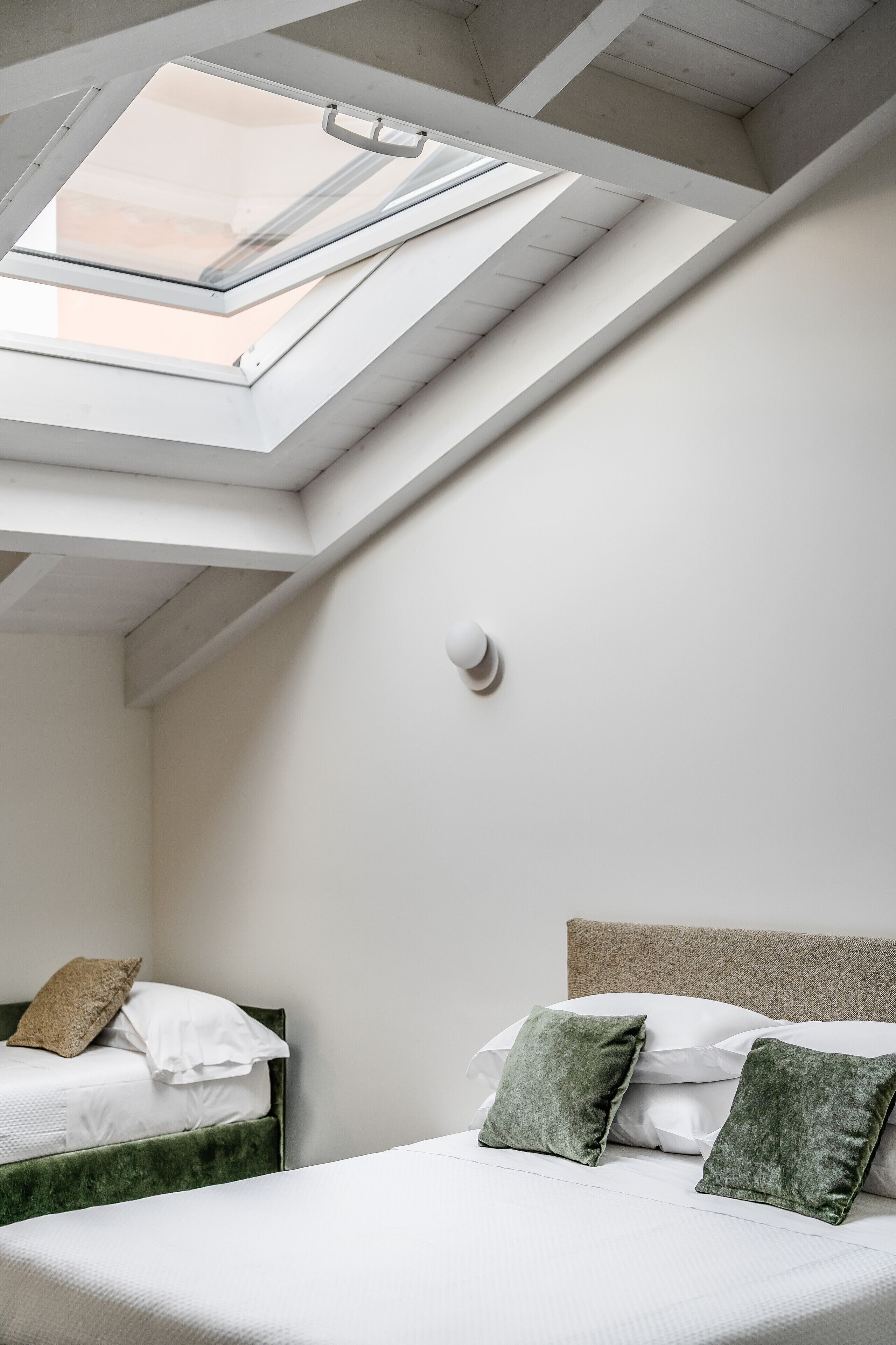 Een slaapkamer met dakraam, een bed met groen en witte beddengoed, en een hoofdbord.