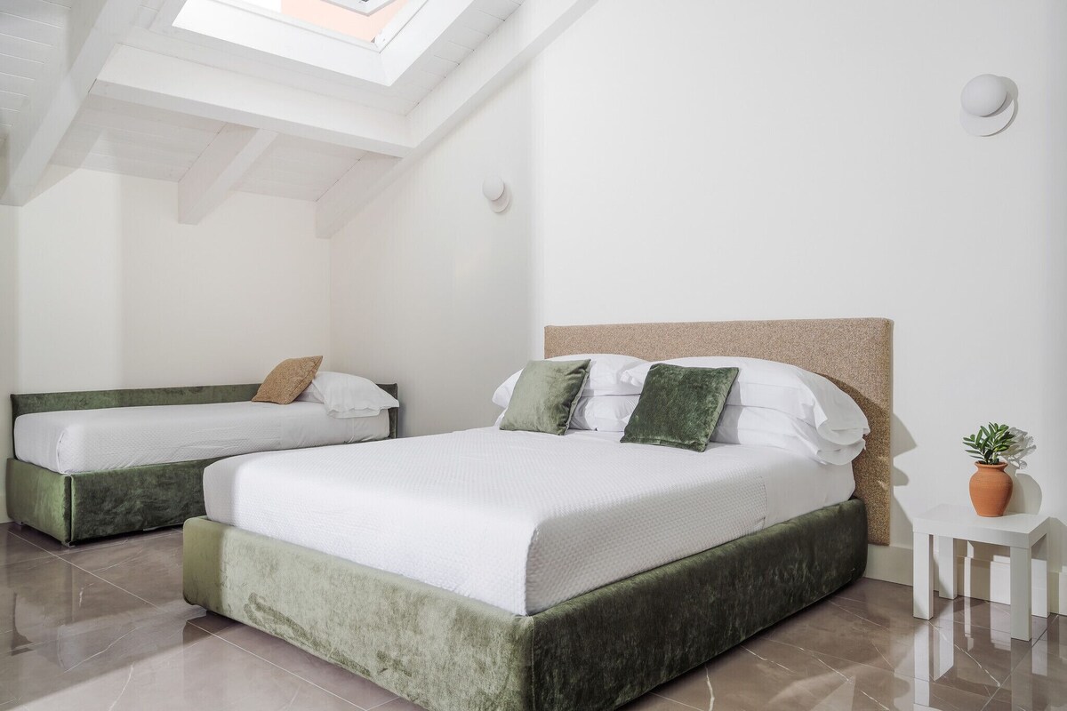 A bedroom with two beds, a skylight, a small table with a plant, and a white wall.