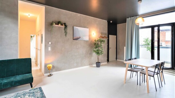 Ein modernes Wohnzimmer mit einer Couch, einem Esstisch mit Stühlen, einer Zimmerpflanze und einem Gemälde an der Wand.