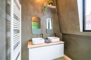 A bathroom with two sinks, a towel, a mirror, and a plant on a shelf. - Antwerp Central Residence2bbknswi-fimic (Antwerp)