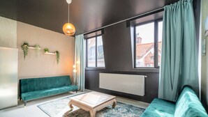 Ein modernes Wohnzimmer mit einem türkisblauen Sofa, einem Couchtisch und einer hängenden Pflanze.