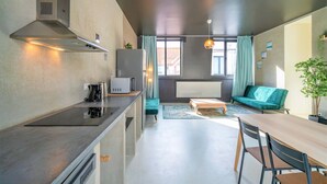 Eine moderne Küche mit Einbauherd, Mikrowelle und Kaffeemaschine. Ein Essbereich mit Holztisch und Stühlen sowie eine Sitzecke mit Sofa.