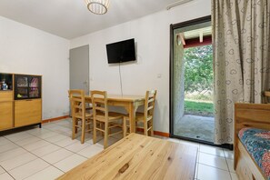 A room with a wooden table, chairs, a TV mounted on the wall, and a sliding glass door leading to an outdoor area.