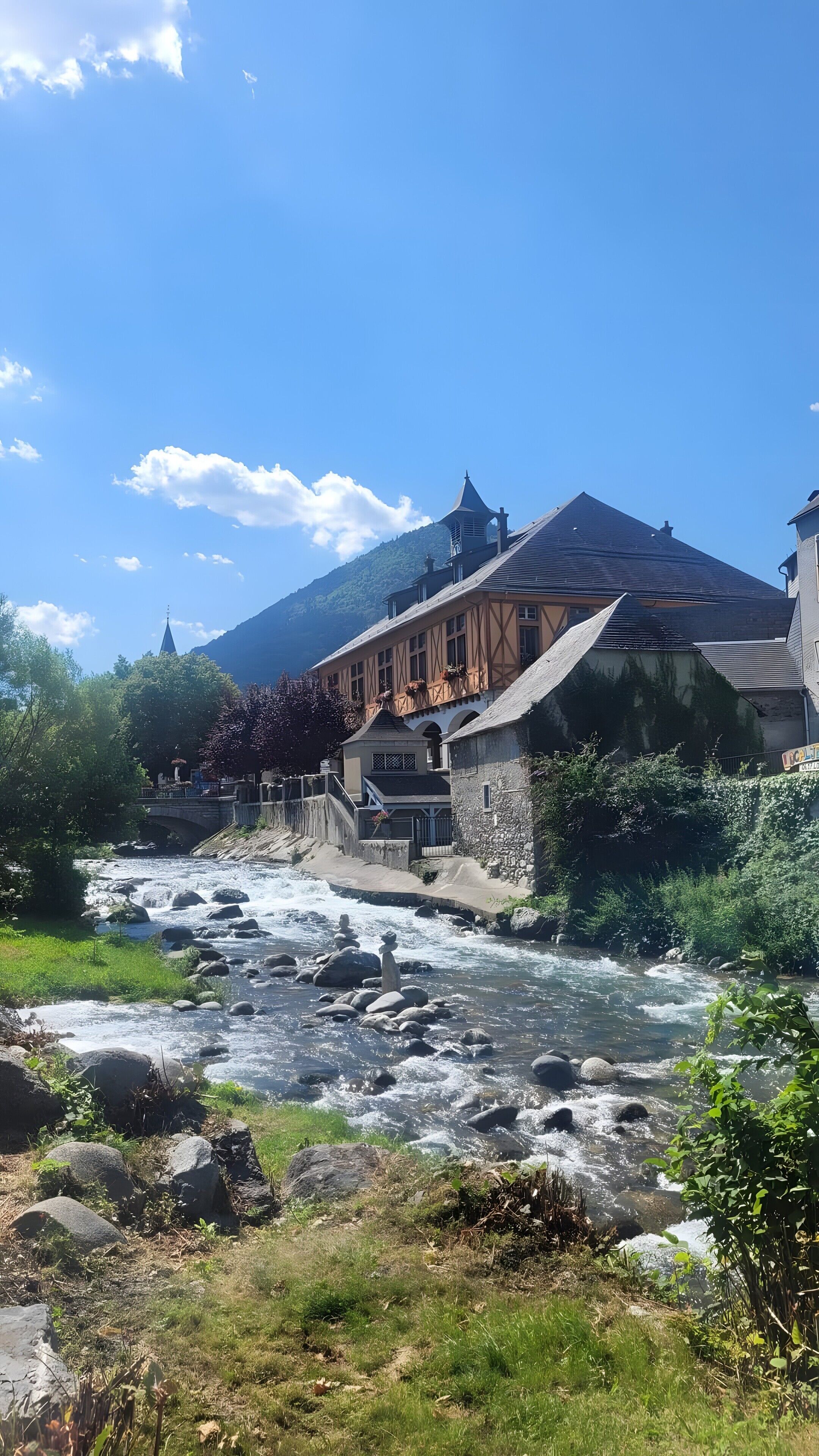 A riverside view with a building featuring a stone facade and a traditional roof.