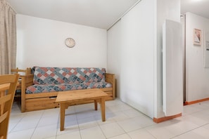 A room with a wooden sofa, a wooden table, a clock on the wall, and a white door.