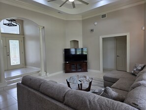 A living room with a sectional sofa, a flat-screen TV on a wooden cabinet, a glass coffee table, and a ceiling fan. - Spacious 4-bedroom home in Laguna Vista w/pool, pickleball, golf course and gym (Laguna Vista)