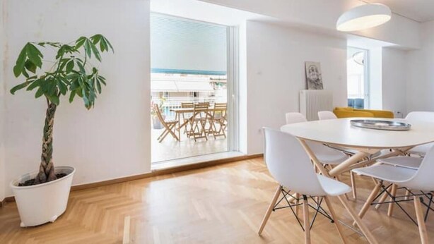 A modern room with a dining table, chairs, a potted plant, and a view through a large window. - Athens Spacious Penthouse - City Center & Metro (Athina)