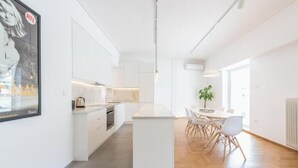 A modern kitchen with white cabinetry, a central island, and a dining area with a table and chairs. - Athens Spacious Penthouse - City Center & Metro (Athina)