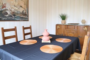 Ein Esstisch mit dunklem Tischtuch, vier gewebten Platzsets, einer rosa Vase und Holzstühlen.