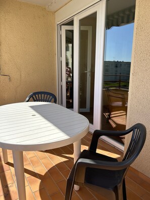 Eine Terrasse mit rundem Tisch und zwei Stühlen, eine Glasschiebetür und im Hintergrund ein Blick auf ein Gebäude.
