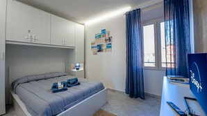 A bedroom with a bed, a desk with a computer, a window with curtains, and a wall with pictures. - [Sea 3m] Trains 8m • A/C • FreeWiFi (Albisola Superiore)
