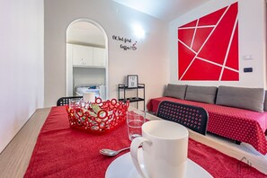 Une pièce moderne aux couleurs rouge et blanche, avec un coin repas agrémenté d’un panier rouge et d’une tasse blanche, un canapé recouvert d’un tissu à pois rouges et un mur orné d’un motif géométrique rouge.