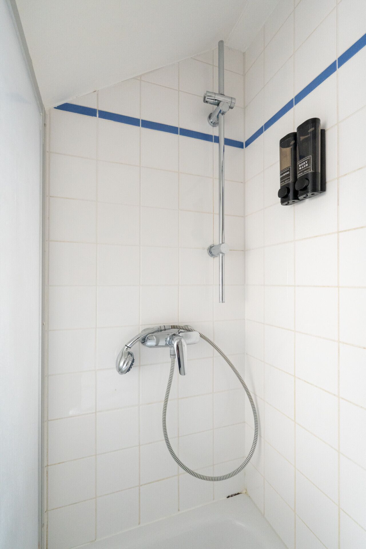 Une douche équipée d’un pommeau de douche à main, d’un robinet mural et d’un flexible de douche à main.