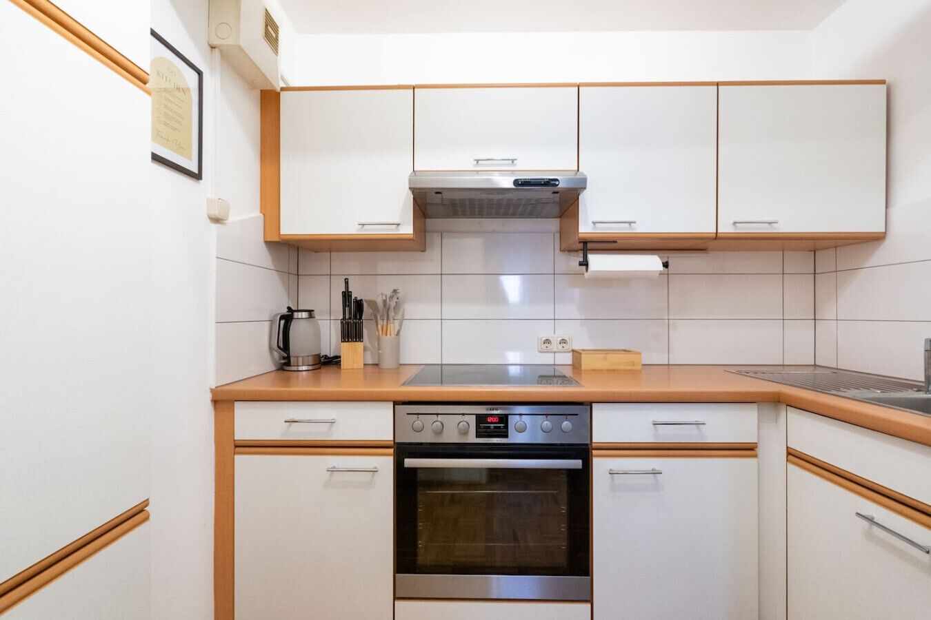 Uma cozinha compacta com armários brancos, forno embutido e coifa de aço inoxidável.