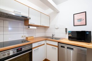 Una cocina moderna con armarios blancos, lavavajillas de acero inoxidable, horno empotrado y microondas.