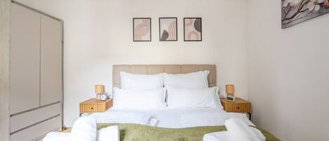 A hotel room with a bed, two bedside tables with lamps, a large wardrobe, and three framed pictures on the wall.