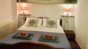 A neatly made bed with decorative pillows, bedside lamps, a radiator, and a framed picture on the wall.
