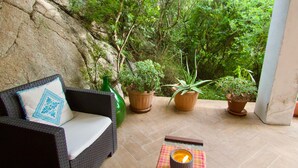 A wicker sofa with a patterned pillow, potted plants, and a candle on a tiled patio.