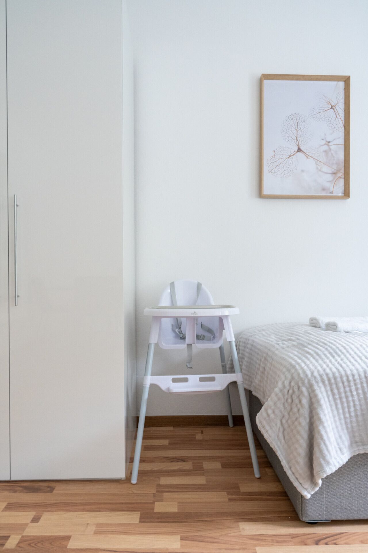 Een slaapkamer met een bed, een witte stoel, een kledingkast en een lijst met een afbeelding aan de muur.