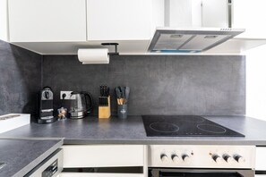 A modern kitchen with a black countertop, a coffee maker, a kettle, and a set of knives. - 55 m² I 2 Rooms I Up to 5 Guests I Near Vienna (Kaltenleutgeben)