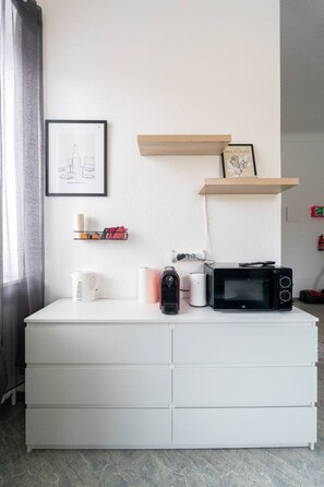 A white dresser with drawers, a framed picture, a shelf with books and a candle, and a microwave on top. - Stylish Apartment at Main Square - 35 m² - Quiet (Leoben)
