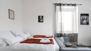 A bedroom with a bed, a sofa, a window with curtains, and two wall-mounted pictures. - Stylish Apartment at Main Square - 35 m² - Quiet (Leoben)