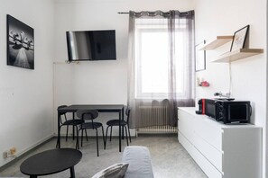 Quarto pequeno e moderno com mesa de jantar, cadeiras, sofá, televisão, radiador e micro-ondas.