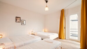 Habitación de hotel con dos camas, una lámpara de techo, una puerta con cortinas amarillas y una ventana.