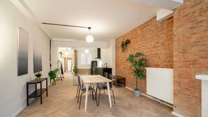 Una cocina moderna con pared de ladrillo, un comedor con mesa y sillas, y un pasillo que lleva a una sala de estar.