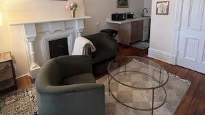 A living room with a fireplace, a sofa, a coffee table, and a kitchen area in the background.
